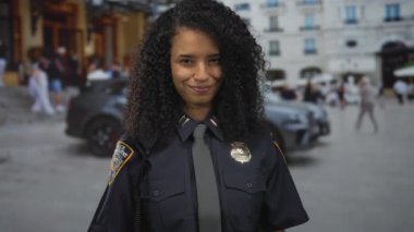 Üniformalı İspanyol kadın polis memuru şehir dışındaki kalabalık sokakta güvenle gülümsüyor. Arabaların geçmişi bulanık ve şehir hayatını temsil eden insanlar var..
