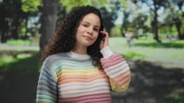 Açık havada güneşli bir günde arka planda ağaçlarla parkın tadını çıkaran renkli kazaklı bir kadın..