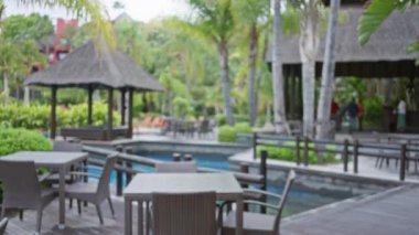 Açık havada bulanık oturma yerleri ve palmiye ağaçları olan tropik bir tesis. Odaklanamayan arka planda lüks ve huzurlu bir ortam sunuyor..