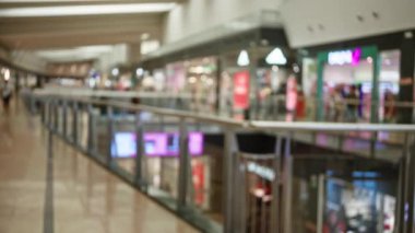 Yoğun bir alışveriş merkezinin bulanık görüntüsü, odaklanmış vitrinler ve arka plandaki insanlar, canlı bir ticari ortamı temsil ediyor..