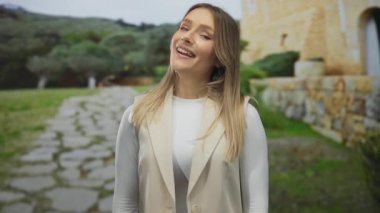 Parkta taş yolu ve yeşilliği olan bir kadın, kırsal manzaranın ortasında tarafsız ifadeler sergiliyor, basitliği ve doğal çevreyi vurguluyor..