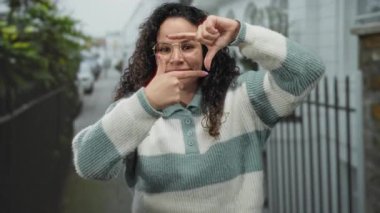 Genç İspanyol kadın gözlük takıyor, sokak ortasında elleri ile bir çerçeve hareketi yapıyor, yaratıcılık ve tarz sergiliyor..