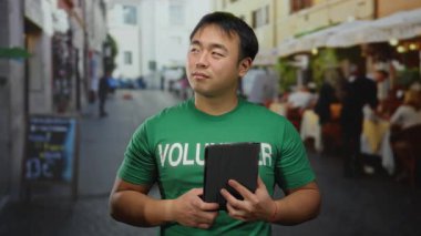 Şehir kafesinde elinde tablet tutan bir adam gönüllü gömlekli, rahat bir atmosfer ve canlı bir şehir hayatı sergiliyor..