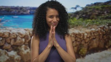 Deniz kenarındaki güvertede güneşli gökyüzünün altında gülümseyen ve rahatlatıcı atmosferiyle neşeli varlığını artıran genç bir kadın..