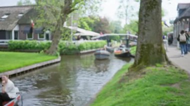 Canlı mavi gökyüzü altında turistler, tekneler, yemyeşil yemyeşil ve geleneksel Hollanda mimarisinin yer aldığı bulanık manzaralı giethoorn kanalları.