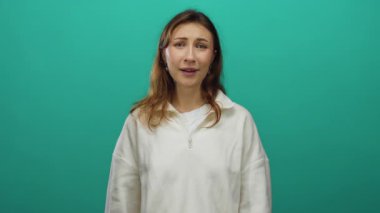 Hislerini günlük kıyafetlerle izole edilmiş yeşil arka plan üzerinde ifade eden genç bir kadın, duygu ve arka plan renklerine vurgu yaparak stok kullanımı için çeşitli yüz ifadeleri yakalıyor..