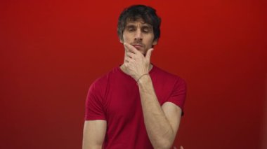 Kırmızı t-shirt giyen adam düşünceli ifade için kırmızı bir stüdyo sahnesinde el ele hareket; düşünme.
