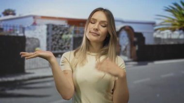 Bir kadın şehir caddesinde uzanan elleri ile düşünüyor, olasılıkları dengeliyor, sarı saç, günlük kıyafetler giyiyor, şehir dışında açık havada, seçenekleri yansıtıyor..