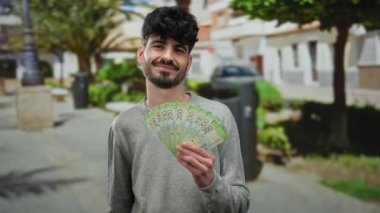 Şehir sokağında elinde Rus banknotları olan bir adam ağaçlar ve bulanık binaları gösteren manzaralı bir arka planda açık havada gülümsüyor..