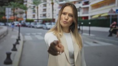 Kalabalık bir caddede el kol gezen genç sarışın bir kadın. Arka planda binalar ve arabalar var. Açık bir şehir ortamında el çabukluğu ve etkileşime işaret ediyor ve davet ediyor.