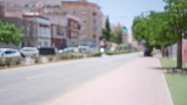 Arka planda araçların, ağaçların ve binaların olduğu bulanık şehir sokak sahnesi, kentsel yaşamın dağıldığını gösteriyor.