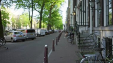 Amsterdam 'da bulanık şehir caddesi manzarası. Buzları çözülmüş ağaçlar, park edilmiş arabalar, bisikletler ve güneşli gün ışığında kaldırım Hollanda' da sakin ve sakin bir atmosfer yaratıyor..