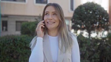 Parkta telefonla konuşan bir kadın... yeşillik ve binalarla dolu, neşeli bir tavır sergiliyor..