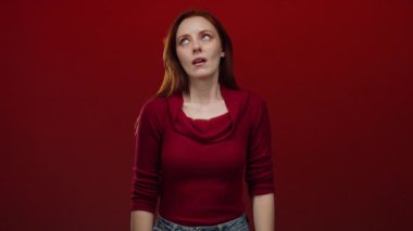 Kadın, neşeli bir yüz ifadesi, hayal kırıklığını ya da bıkkınlığı yansıtan canlı kırmızı bir arkaplan karşısında parmak tabancası hareketi yapıyor..