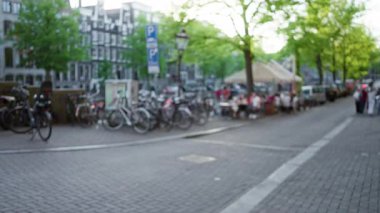 Bisikletler Hollanda 'da ağaçların altında bulanık insanların yemek yediği bokeh dolu bir sokak hizasında. Canlı bir şehir manzarası gözler önüne seriliyor..