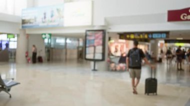 Bulanık bir adam, yoğun bir zamanda seyahat ederken, arka planda bavuluyla havalimanında yürüyordu..