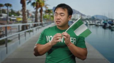 Deniz kenarındaki gezinti güvertesinde Nijerya bayrağı taşıyan genç bir adam, gerginliğini dile getiriyor, plaj kenarında açık havada gönüllü gömleği giyiyor..