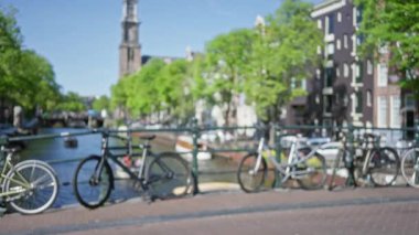 Hollanda 'nın dağılmış, bokeh bir sahnesinde Amsterdam' da canlı yeşillik ve tarihi mimari sergilenen bir kanalın üzerindeki köprüde park edilmiş bulanık bisikletler..