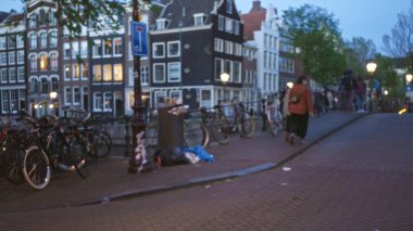 Amsterdam 'da bir kanal boyunca yürüyen insanların bulanık manzarası. Akşam gökyüzünün altında bisikletlerle ve tarihi binalarla çevrili. Hollanda' da Bokeh etkisi var..