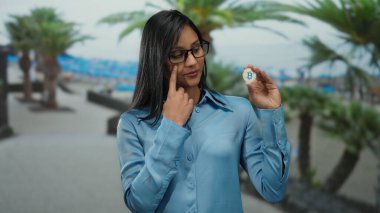 Plaj arka planında Bitcoin tutan kadın açık havada dijital para birimi vurguluyor açık hava teknolojisi ve finans kavramlarını vurgulayan mavi gömlekli..