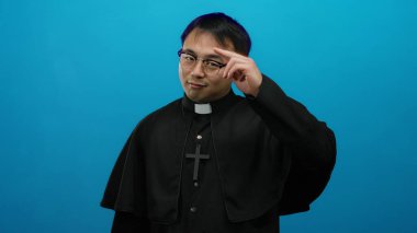 Mavi arka plana poz veren rahip kıyafeti giyen adam güven verici bir dini kavrama işaret ediyor. Jest ve ifade yoluyla güven ve inanca ilham veriyor..