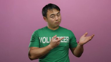 Yeşil gönüllü gömleği giyen genç adam, dışlanmış pembe arka plana karşı anlamlı bir pozda duruyor..