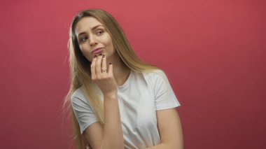 Beyaz gömlek giyen, düşünceli bir ifade sergileyen, gençlik merakını ve iç gözlem anlayışını ön plana çıkaran canlı kırmızı arka planı olan bir kadın..