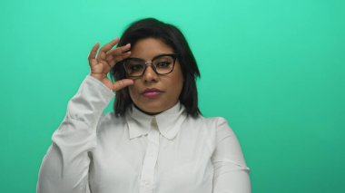 Gözlüklerini yeşil arka plana göre ayarlayan, beyaz gömlek giyen, büyük beden giyen, yalıtılmış ortamda Latin güzelliğini gösteren, modern tarz ve güç veren bir kadın..