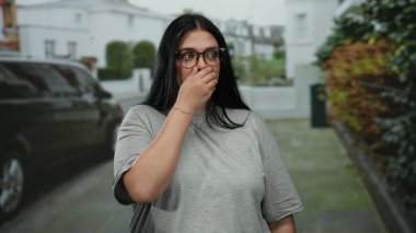 Gözlüklü bir kadın şehir caddesinde şaşkın ve meraklı bir şekilde duruyor, şehir dışı yaşam tarzını ve duygularını gelişigüzel bir şekilde yakalıyor..