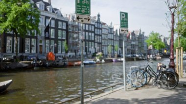 Klasik bina ve ağaçlarla dolu bulanık bir kanal boyunca park etmiş bisikletler Hollanda kentsel manzarasının özünü tasvir eden rüya gibi bir bokeh etkisi yaratıyor..