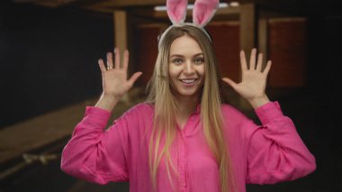 Pembe tişörtlü, tavşan kulaklı bir kadın. İnşaat alanında gülümsüyor. Neşeli ve genç bir hava sergiliyor..