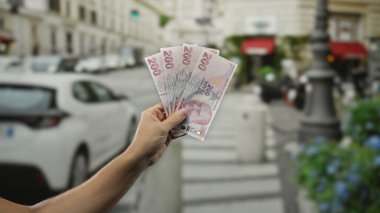 Elinde Türk lirası banknotları olan bir adam, şehir yaşamının ortasında mali refah sergiliyor..