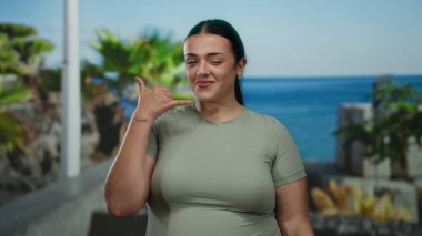 Bana işaret eden bir kadın, yeşil gömlekli, gülümseyen, açık hava, tropikal ortam, gündüz kuşağı, neşeli, rahat atmosfer..