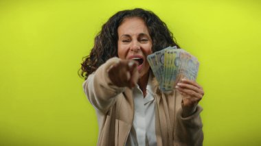Romanyalı banknotları canlı sarı bir arka planda tutan kadın, neşeli bir ifadeyle para gösterirken enerjik bir şekilde ileriye bakıyor..