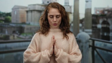 Roma harabelerinde sakince meditasyon yapan, rahat süveter giyen, eski şehir zeminine karşı duruş sergileyen, tarihi mimarinin ortasında sükuneti anımsatan bir kadın..