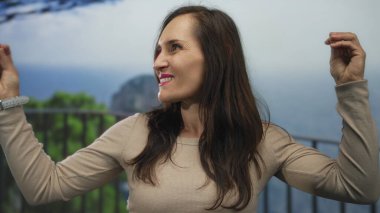 Genç İspanyol kadın elleri deniz kenarında hareketli jest yapıyor; iletişim tutkusunu ifade ediyor.