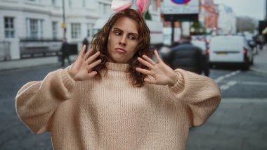 Kazak giymiş tavşan kulaklı bir kadın, arka planda arabalar ve binalarla dolu bir şehir caddesinde şakacı şakalar yapıyor..