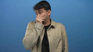 Erkek ağzı arka planda elle kaplanırken İspanyol genç mavi gülüyor utangaç adam şakacı tepki veriyor..