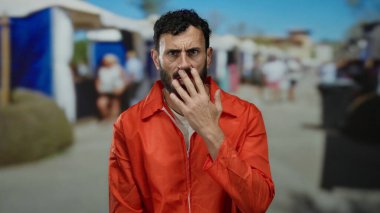 Portakal rengi hapishane tulumlu İspanyol adam kalabalık bir sokakta endişeli görünüyor, düşünceli bir ifadeyle yüzüne dokunuyor..