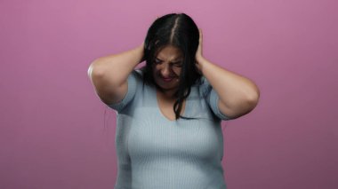 Gözleri kapalı bir kadın stresle kulaklarını kapatıyor. Canlı pembe duvarlara karşı izole edilmiş. Hayal kırıklığı ya da gürültü öneriyor..