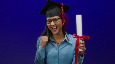 İzole edilmiş mavi bir arka planda diplomayla kutlama yapmış, neşe ve başarı gösteren bir kadın..