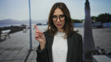 Açık gökyüzü ve okyanus manzaralı güneşli bir sahil geçidinde, gözlüklü ve rahat bir sahil atmosferi sergiliyor..