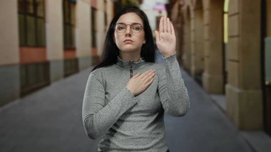 Sessiz bir sokakta yemin eden gözlüklü bir kadın açık havada ciddi bir bağlılık gösteriyor.