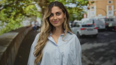 Genç sarışın kadın yüzü, çizgili bluz içinde dalgalı saçlarıyla gülümsüyor yapraklı güneş ışığı kaldırımında; keyif güveni.