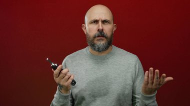 Sakallı kafası karışmış kel bir adam arabanın anahtarlarını kırmızı duvarda tutarken düşünceli bir poz vermiş..