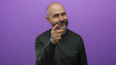 Mor arka planda sakallı kel bir adam. El işaretleri ve dövmesi ile ihtiyatlı olduğunu söylüyor..