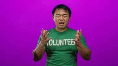 Asyalı bir adam yeşil gönüllü gömleği giyiyor. Canlı pembe izole edilmiş arka plana karşı duygusal görünüyor. Hayal kırıklığını ifade ediyor ve enerjik bir şekilde poz veriyor..