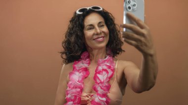 Mayolu İspanyol kadın ve Lei, izole olmuş kahverengi bir duvara selfie çekiyorlar. Orta yaşlı neşeli bir yaz havası sergiliyorlar..