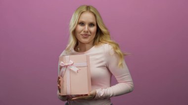 Pembe bir hediye kutusunu canlı pembe bir arka planda tutarken gülümseyen bir kadın neşeli ve neşeli bir atmosfer sergiliyor. Kutlama ya da tatil teması için mükemmel..