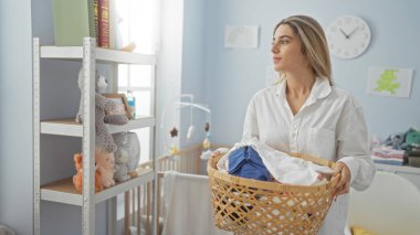 Çamaşır odasında çamaşır sepeti tutan kadın, günlük kıyafetler giymiş, iç dekorasyonla çevrili, ev temizliği ve günlük ev işleri sergiliyor..